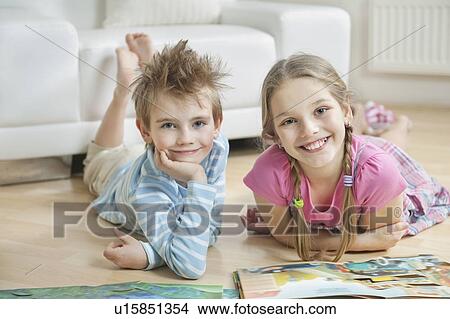 Picture - Portrait of happy siblings with story books lying on floor in living room. Fotosearch