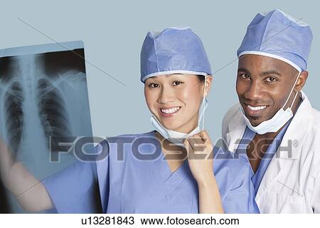Stock Image - Portrait of happy surgeons holding x-ray report over light blue background. Fotosearch