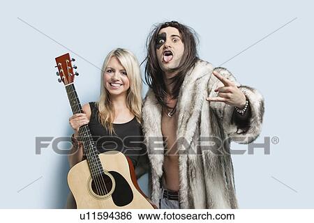Stock Photograph - Portrait of happy young man gesturing with woman holding guitar against light blue background. Fotosearch