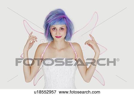 Stock Photo - Portrait of happy young woman dressed as angel with dyed hair against gray background. Fotosearch