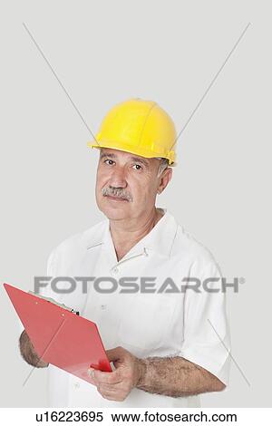 Portrait of senior constructor standing with clipboard over gray background View Large Photo Image Stock Photography - Portrait of senior constructor standing with clipboard over gray background. Fotosearch