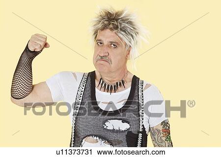 Stock Image - Portrait of senior male punk showing clenched fist over yellow background. Fotosearch