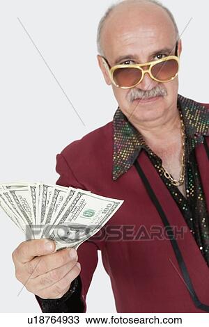 Stock Image - Portrait of senior man showing US banknotes against gray background. Fotosearch