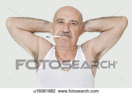 Stock Image - Portrait of senior man with hands behind head and cigarette in mouth over gray background. Fotosearch