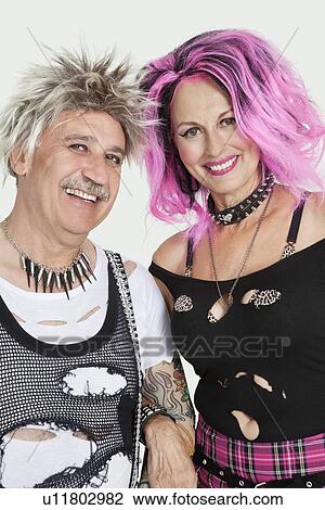 Stock Image - Portrait of senior punk couple standing with arm in arm over gray background. Fotosearch