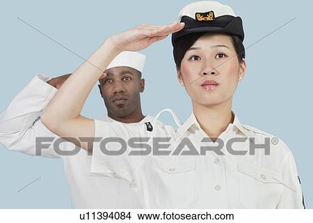 Picture - Portrait of serious female US Navy officer and male sailor saluting over light blue background. Fotosearch