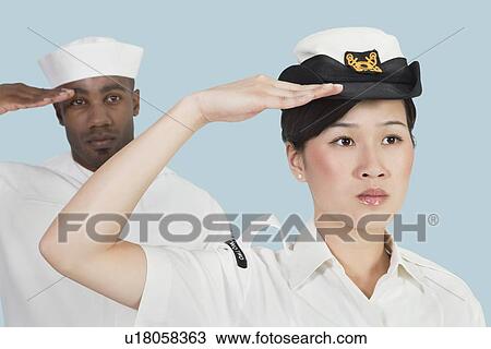 Stock Image - Portrait of serious female US Navy officer and male sailor saluting over light blue background. Fotosearch