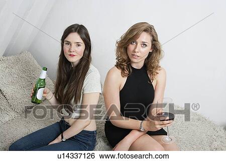 Portrait of two young women having drinks while sitting on sofa View Large Photo Image Stock Photograph - Portrait of two young women having drinks while sitting on sofa. Fotosearch