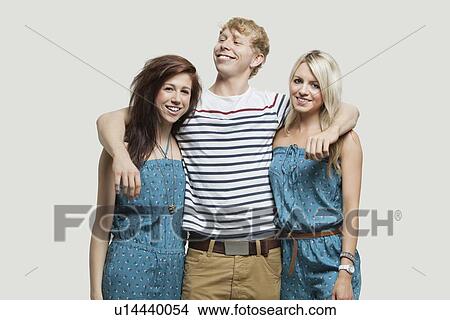 Portrait of two young women in similar jumpsuits standing with happy male friend over gray background View Large Photo Image Picture - Portrait of two young women in similar jumpsuits standing with happy male friend over gray background. Fotosearch