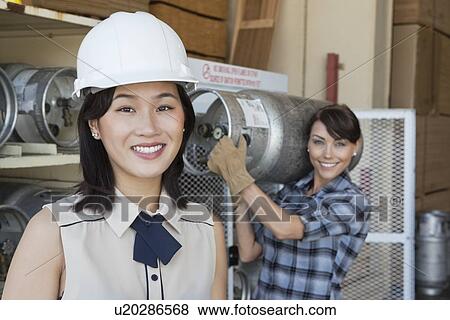Portrait of woman smiling with female industrial worker carrying propane cylinder in background View Large Photo Image Stock Photo - Portrait of woman smiling with female industrial worker carrying propane cylinder in background. Fotosearch