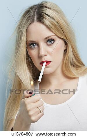 Portrait of young blond woman igniting cigarette against light blue background View Large Photo Image Stock Photo - Portrait of young blond woman igniting cigarette against light blue background. Fotosearch