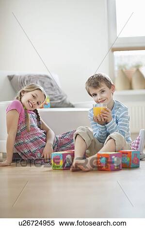 Portrait of young boy drinking orange juice while sitting with sister on floor View Large Photo Image Stock Photography - Portrait of young boy drinking orange juice while sitting with sister on floor. Fotosearch