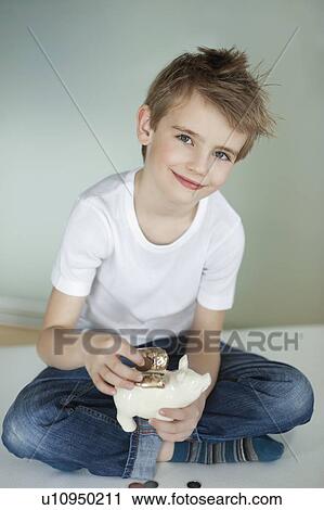 Stock Image - Portrait of young boy putting coin in piggy bank. Fotosearch