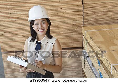Portrait of young female industrial worker writing on clipboard with wooden planks in background View Large Photo Image Stock Photo - Portrait of young female industrial worker writing on clipboard with wooden planks in background. Fotosearch