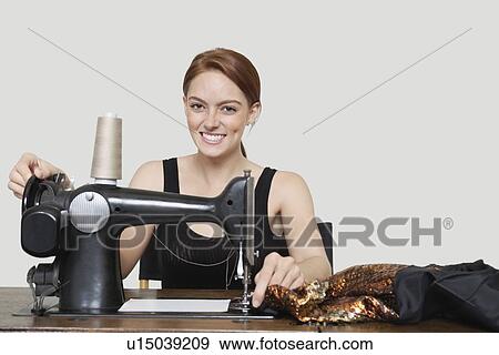 Stock Photo - Portrait of young female tailor stitching cloth on sewing machine over colored background. Fotosearch