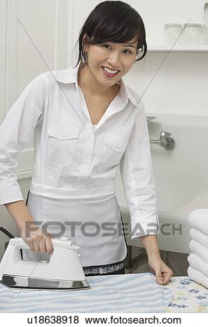 Stock Photo - Portrait of young housemaid ironing shirt. Fotosearch