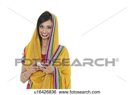 Portrait of young Indian woman in traditional wear holding cell phone against white background View Large Photo Image Stock Photograph - Portrait of young Indian woman in traditional wear holding cell phone against white background. Fotosearch