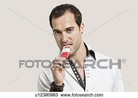 Portrait of young man eating ice cream candy against gray background View Large Photo Image Stock Image - Portrait of young man eating ice cream candy against gray background. Fotosearch