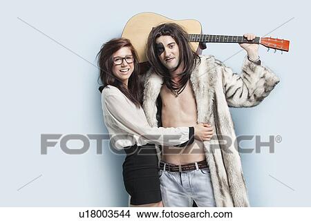 Picture - Portrait of young man holding guitar while standing with happy woman against light blue background. Fotosearch