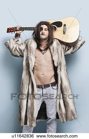 Stock Photograph - Portrait of young man in fur coat holding guitar against light blue background. Fotosearch