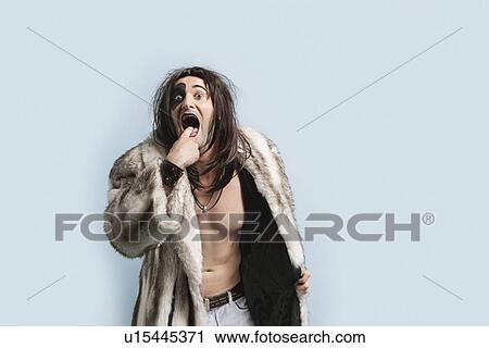 Portrait of young man in fur coat with finger in mouth standing against light blue background View Large Photo Image Stock Image - Portrait of young man in fur coat with finger in mouth standing against light blue background. Fotosearch