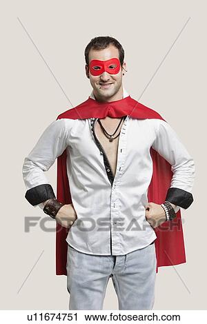 Stock Image - Portrait of young man in superhero costume with hands on hip standing against gray background. Fotosearch