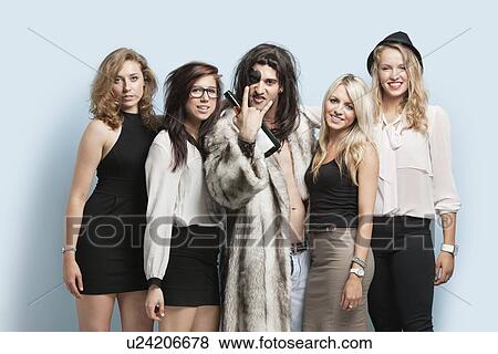 Portrait of young man making rebellious gestures while standing with women against light blue background View Large Photo Image Stock Photo - Portrait of young man making rebellious gestures while standing with women against light blue background. Fotosearch