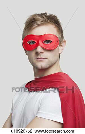Stock Image - Portrait of young man wearing superhero costume against gray background. Fotosearch