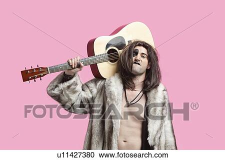 Stock Image - Portrait of young man with attitude holding guitar on shoulder over pink background. Fotosearch