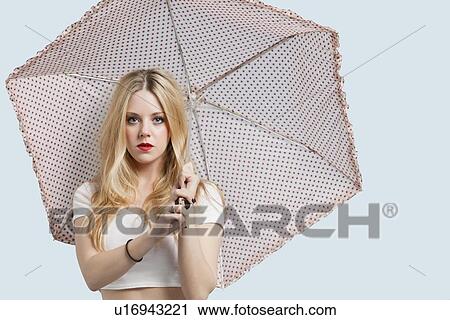 Portrait of young woman holding polka dotted umbrella against light blue background View Large Photo Image Stock Image - Portrait of young woman holding polka dotted umbrella against light blue background. Fotosearch