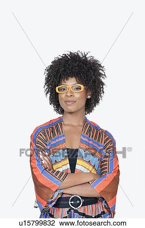 Stock Image - Portrait of young woman in African print attire standing hands folded over gray background. Fotosearch