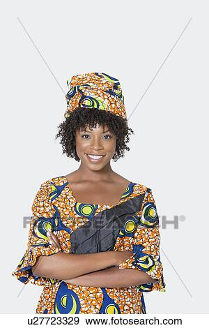 Stock Photo - Portrait of young woman in African print attire standing arms crossed over gray background. Fotosearch