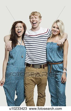 Stock Image - Portrait of young woman standing with cheerful friends against gray background. Fotosearch