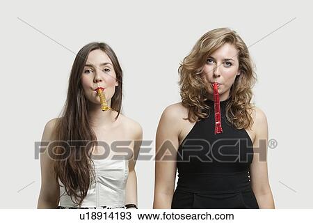 Portrait of young women blowing party puffers against gray background View Large Photo Image Stock Image - Portrait of young women blowing party puffers against gray background. Fotosearch