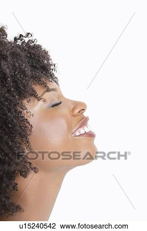 Stock Image - Profile view of an African American woman smiling with eyes closed against gray background. Fotosearch