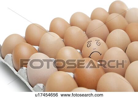 Stock Photograph - Sad face drawn on an egg surrounded by plain brown eggs in carton against white background. Fotosearch