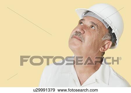 Stock Photo - Senior construction worker with hardhat looking up over yellow background. Fotosearch