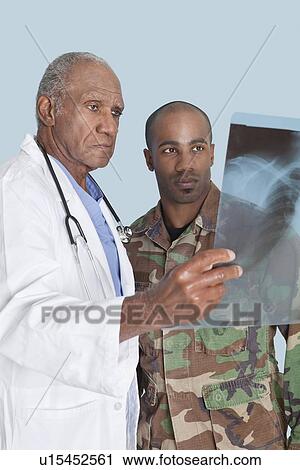 Senior doctor with US Marine Corps soldier looking at x-ray report over light blue background View Large Photo Image Stock Image - Senior doctor with US Marine Corps soldier looking at x-ray report over light blue background. Fotosearch