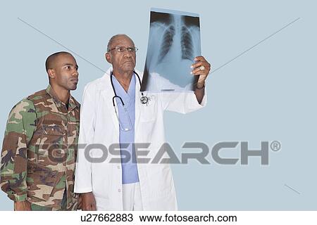 Senior doctor with US Marine Corps soldier looking at x-ray report over light blue background View Large Photo Image Stock Image - Senior doctor with US Marine Corps soldier looking at x-ray report over light blue background. Fotosearch