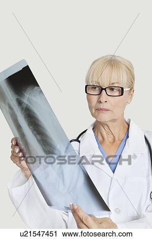 Stock Image - Senior female doctor examining x-ray over gray background. Fotosearch