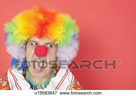 Senior male clown sticking out tongue while looking away over red background View Large Photo Image Stock Photo - Senior male clown sticking out tongue while looking away over red background. Fotosearch