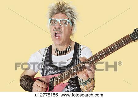 Stock Photograph - Senior male punk musician playing guitar over yellow background. Fotosearch