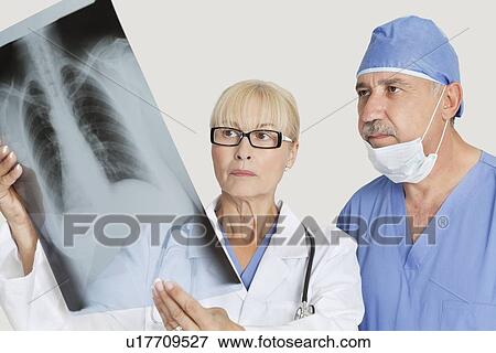 Stock Photo - Senior male surgeon and female doctor looking at x-ray over gray background. Fotosearch