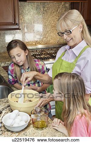 Stock Photograph - Senior woman with granddaughters mixing batter in kitchen. Fotosearch