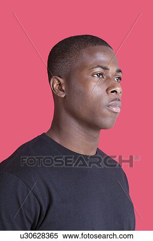 Stock Photography - Serious African American young man looking away over pink background. Fotosearch