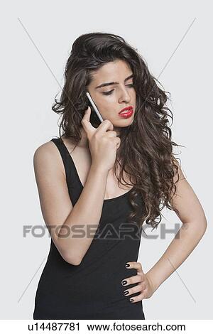 Stock Image - Serious young woman using cell phone over gray background. Fotosearch