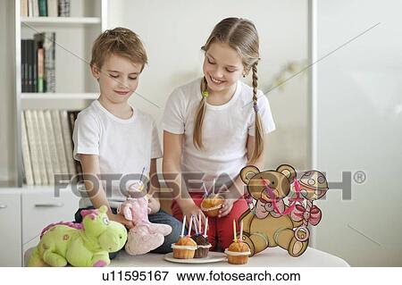 Stock Photo - Siblings and soft toys celebrating birthday with cup cakes. Fotosearch