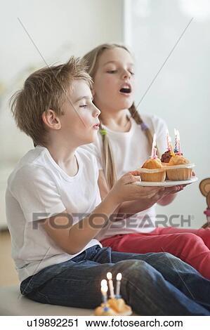 Stock Image - Siblings blowing candles on cupcakes. Fotosearch