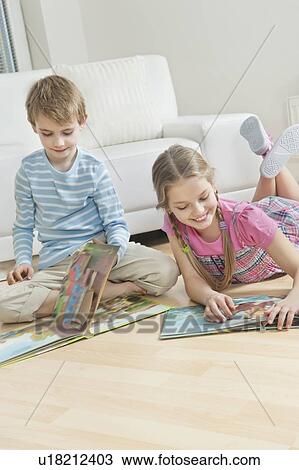 Stock Image - Siblings reading story books on floor in the living room. Fotosearch