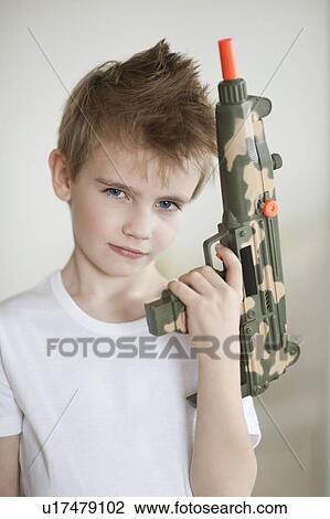 Stock Image - Side view of a young boy holding toy gun. Fotosearch